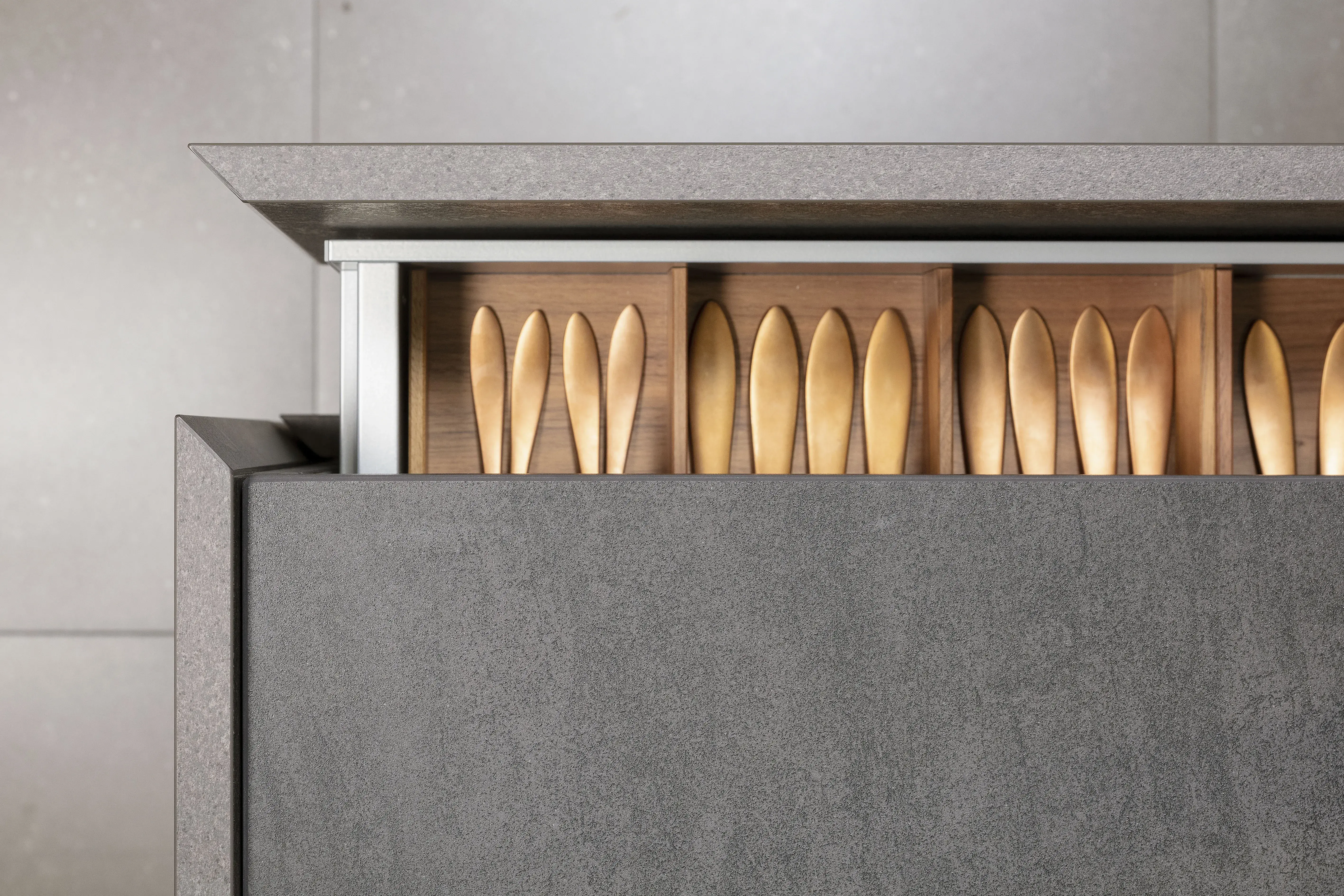 Besteckschublade mit Holzfächern und goldfarbenem Besteck in moderner Küche.